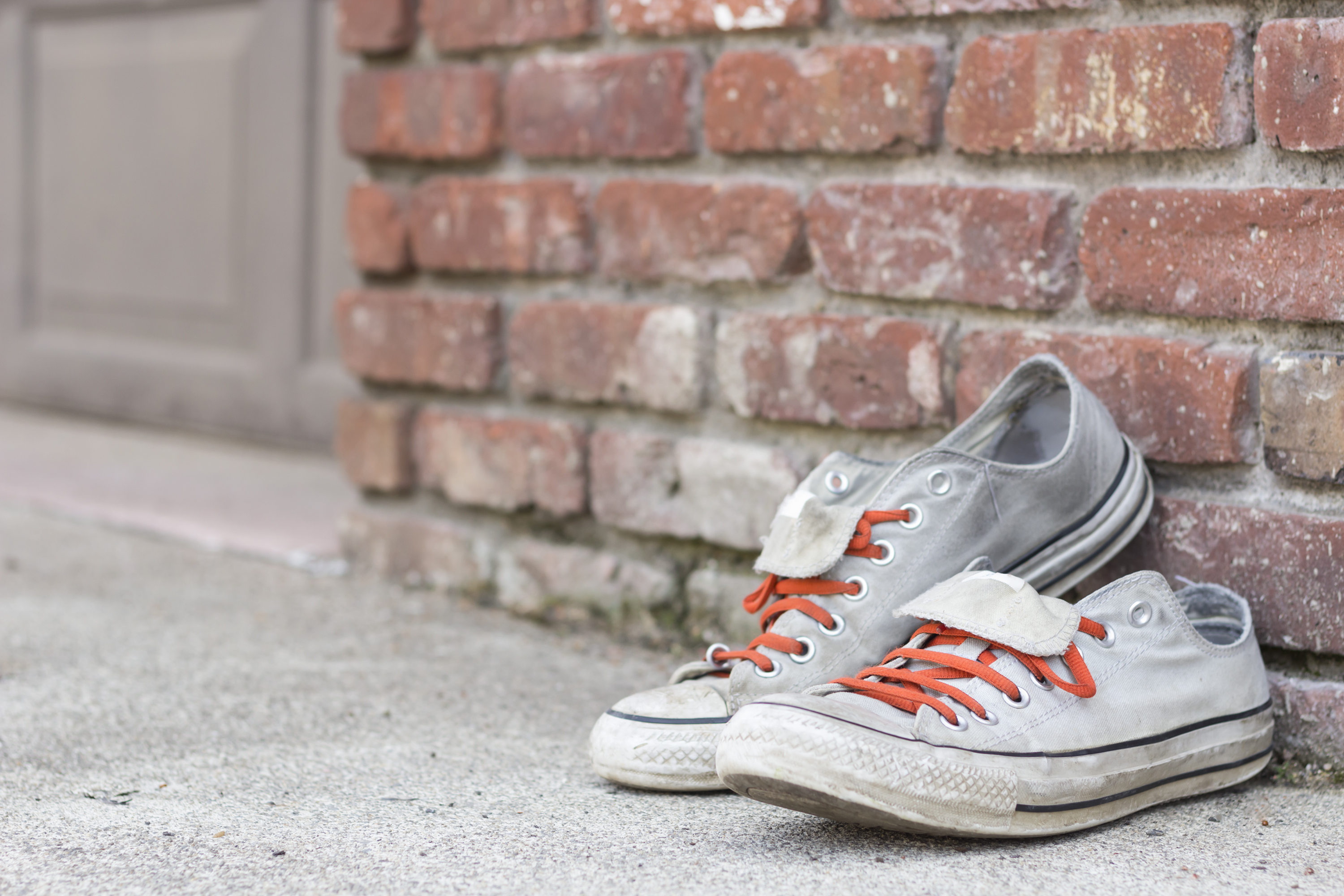 Pair of old worn classic sneakers leaning against a brick wall